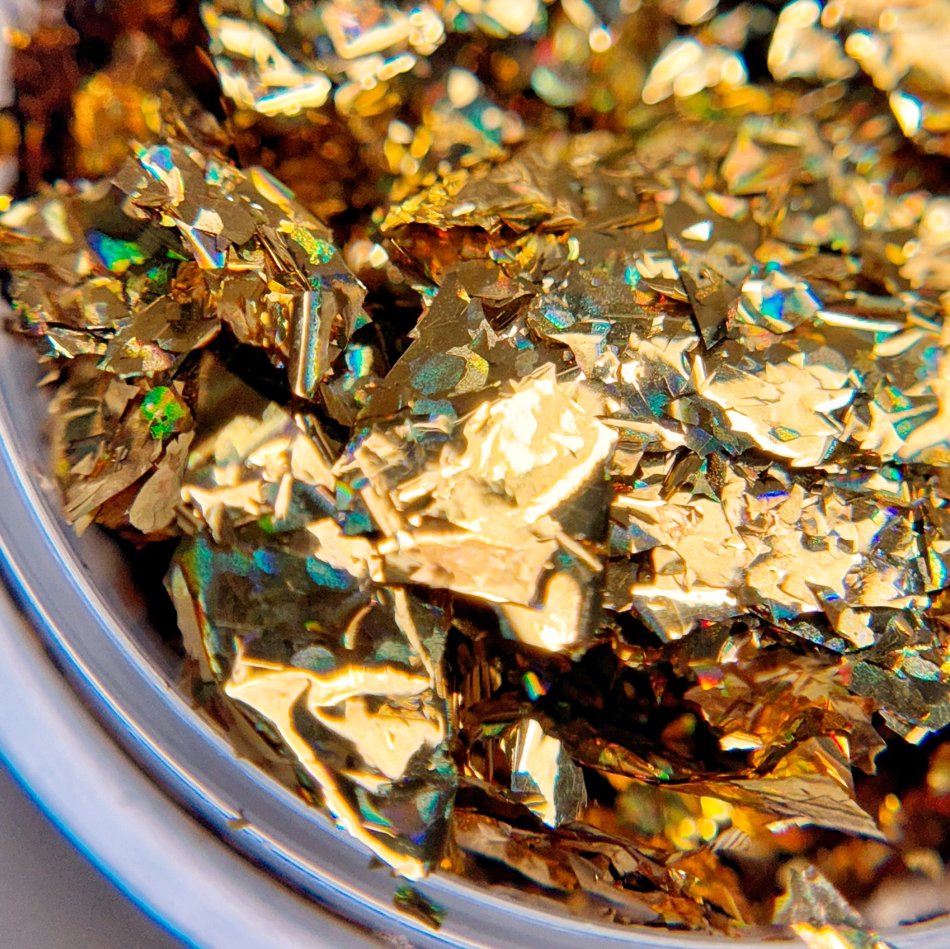 A close-up image of gold-colored glitter flakes, intended for nail art.
