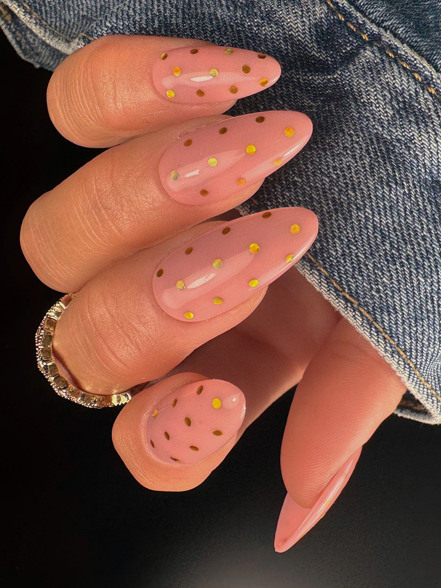 Nail art with pink polish and gold polka dots on a dark background