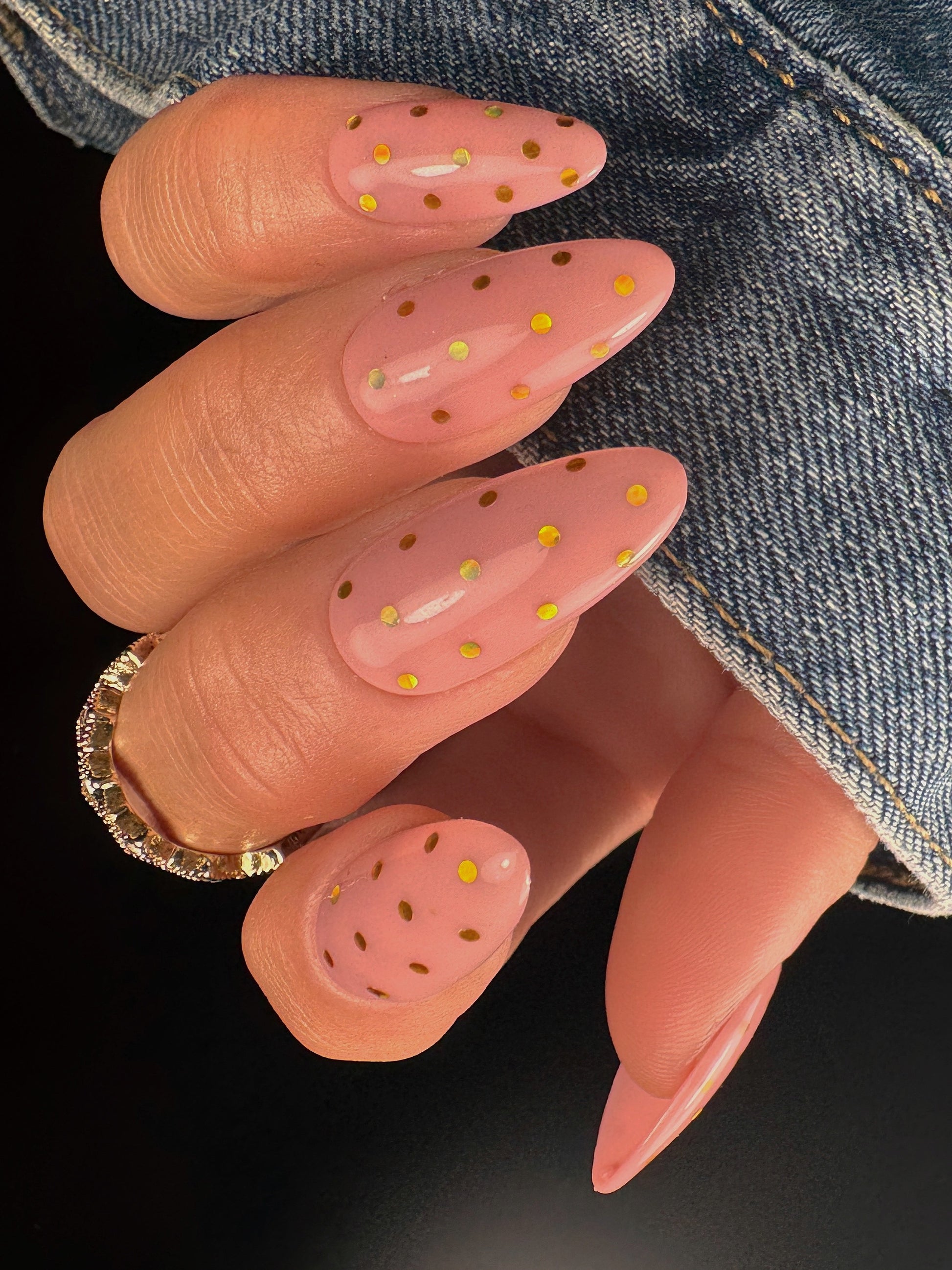 Nail art with pink polish and gold polka dots on a dark background