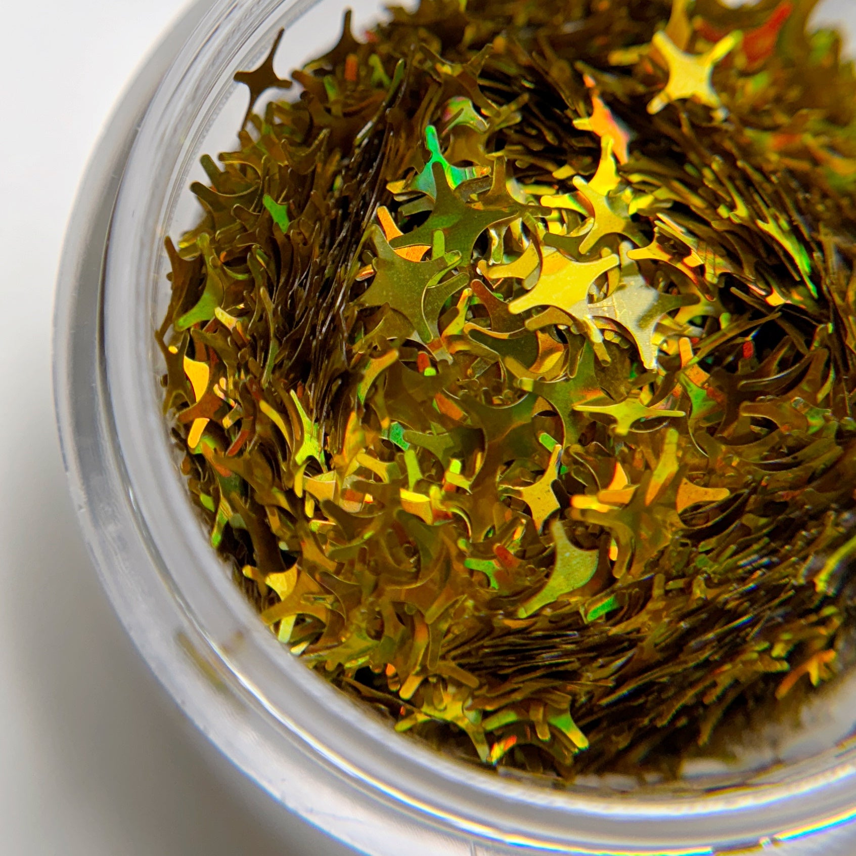 A close-up image of a jar containing gold holographic star-shaped glitter pieces.