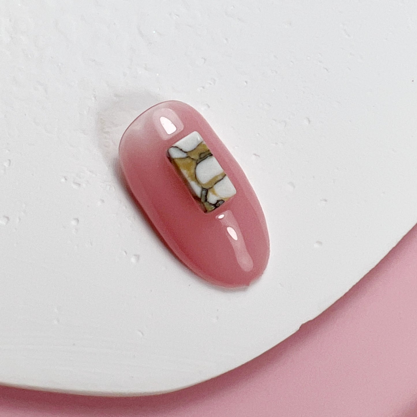 Decorated nail tip on white textured surface with pink background