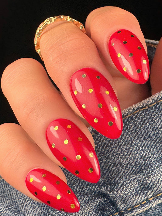 Red nail art with gold polka dots on a person's hand wearing denim jeans.