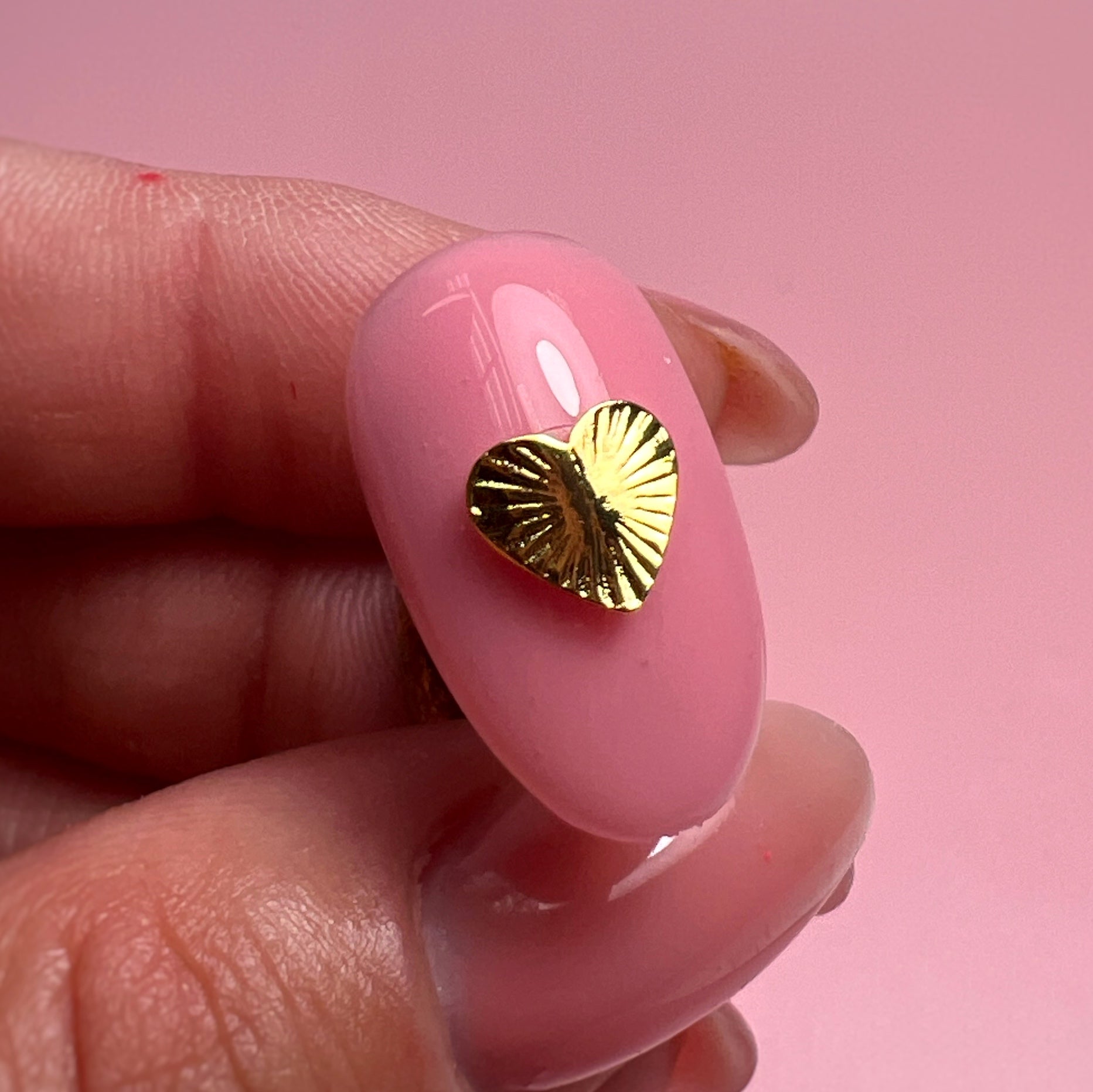 Gold heart-shaped nail art design on a pink nail with a pink background