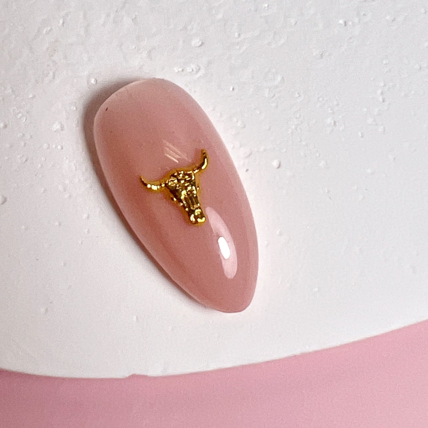 Pink nail with a gold bull design on a white background