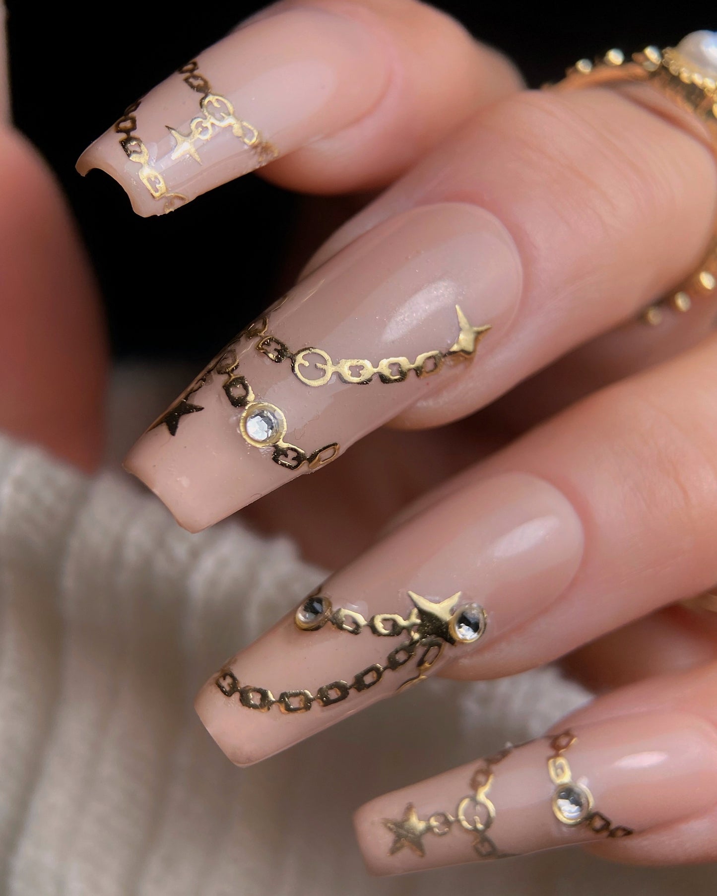 Nails with gold chain and star designs on a neutral background