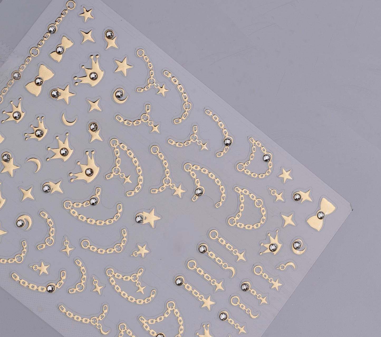 Sheet of gold jewelry stickers with chains, stars, and bows on a gray background