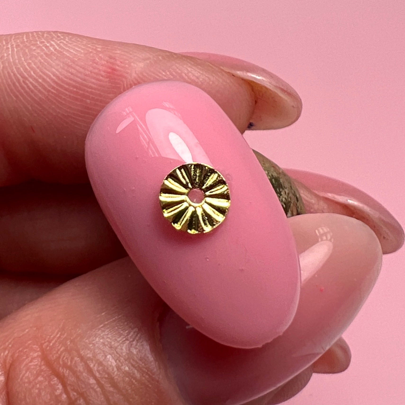 Hand holding decorated nail tip against pink background.