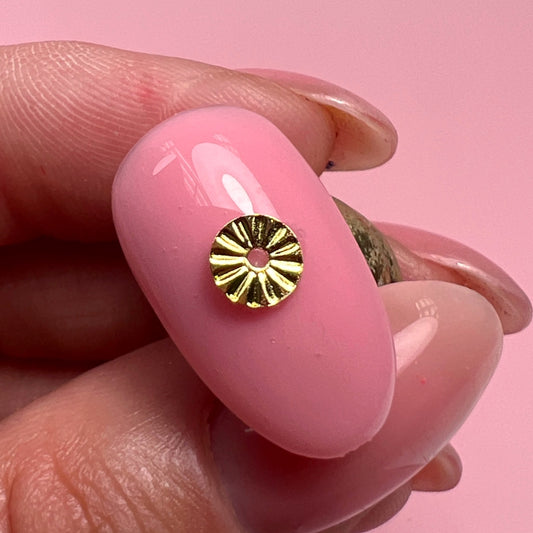 Hand holding decorated nail tip against pink background.