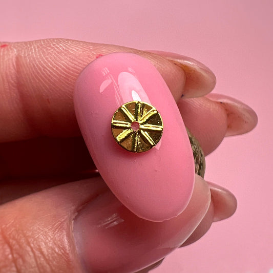 Gold circular charm on a pink nail against a pink background
