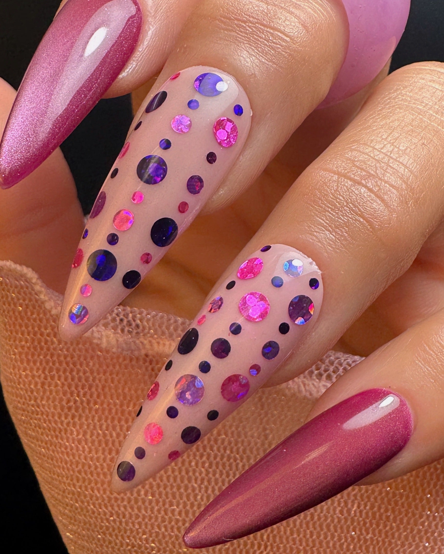 Nails with pink and purple polka dot design on a dark background