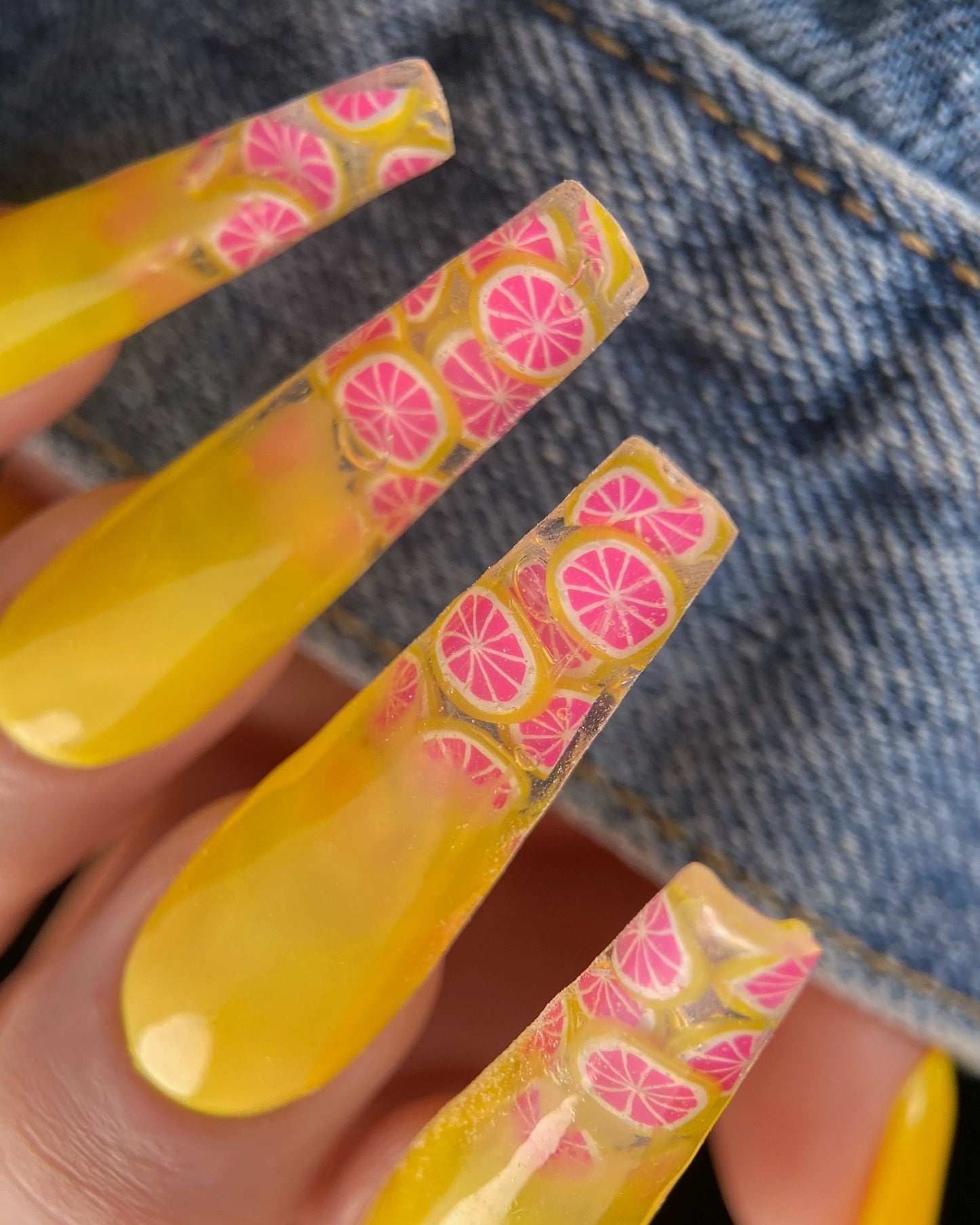 Yellow nail polishes with pink and orange pattern on a denim background