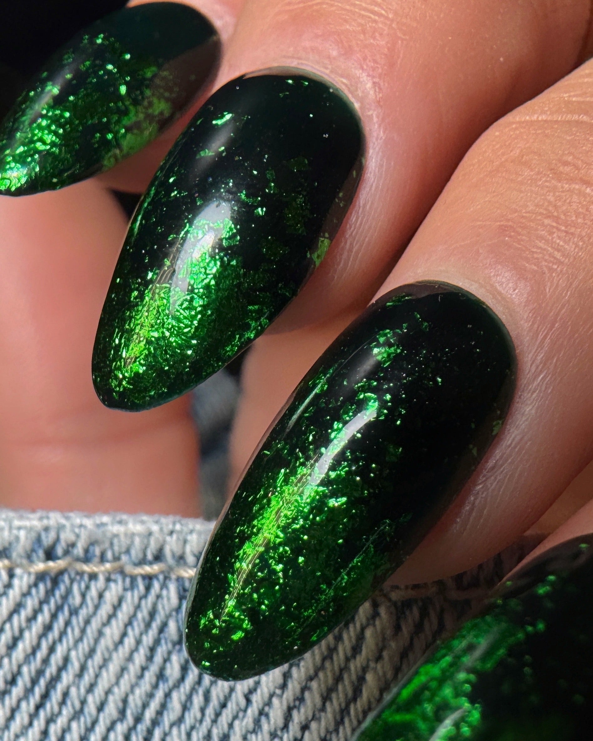 Close-up of a hand with green glittery nail art on a blurred denim background