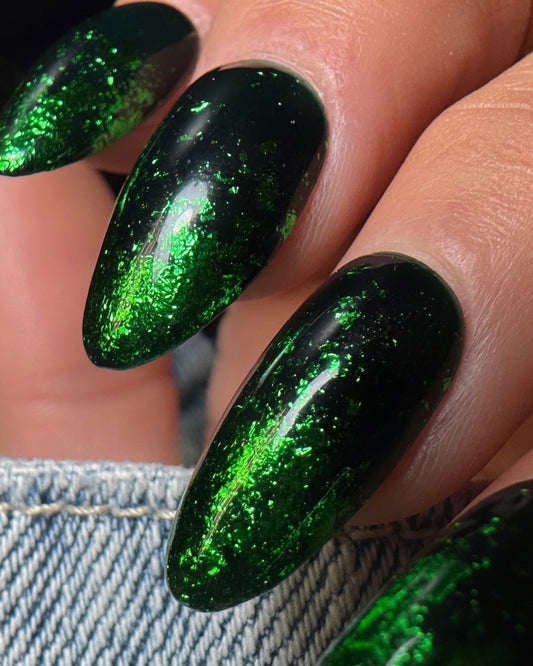 Close-up of a hand with green glittery nail art on a blurred denim background