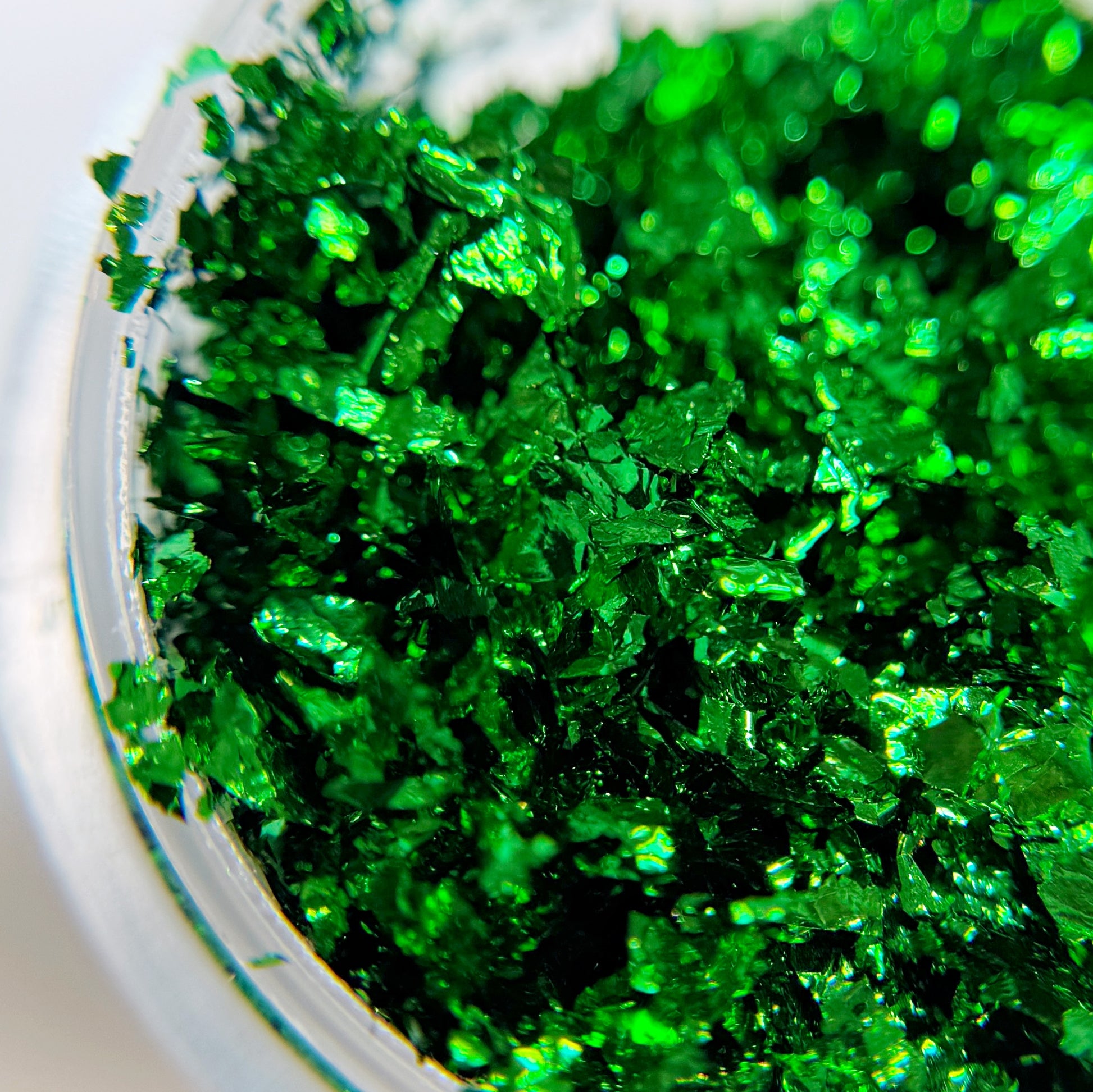 A close-up view of green metallic nail flakes in jar on blurred background.