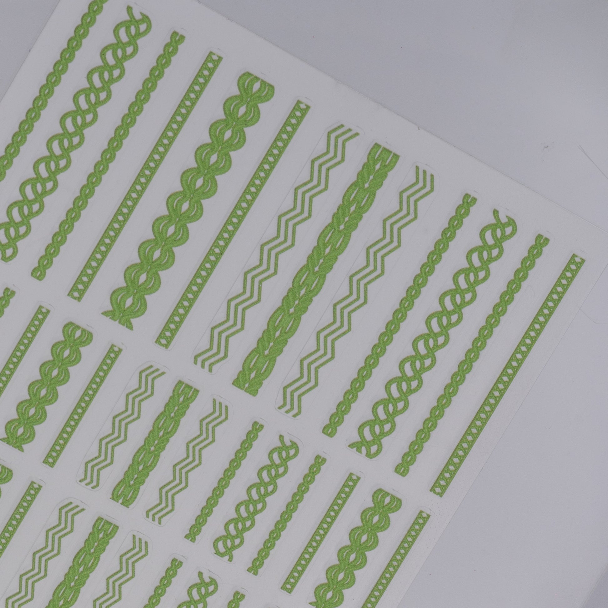 Sheet of green nail stickers with various designs on a white background
