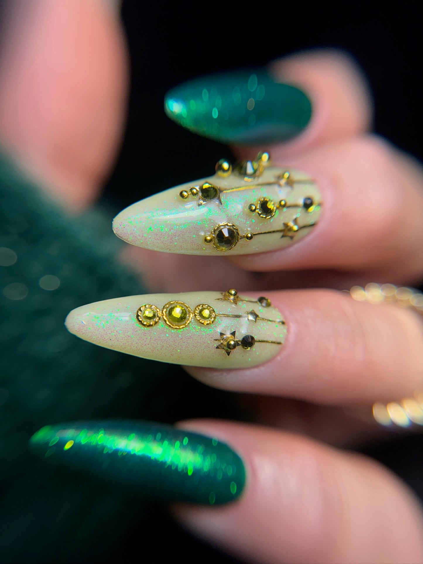 Close-up of a hand with decorative nails featuring gold studs and green glitter and gel polish.