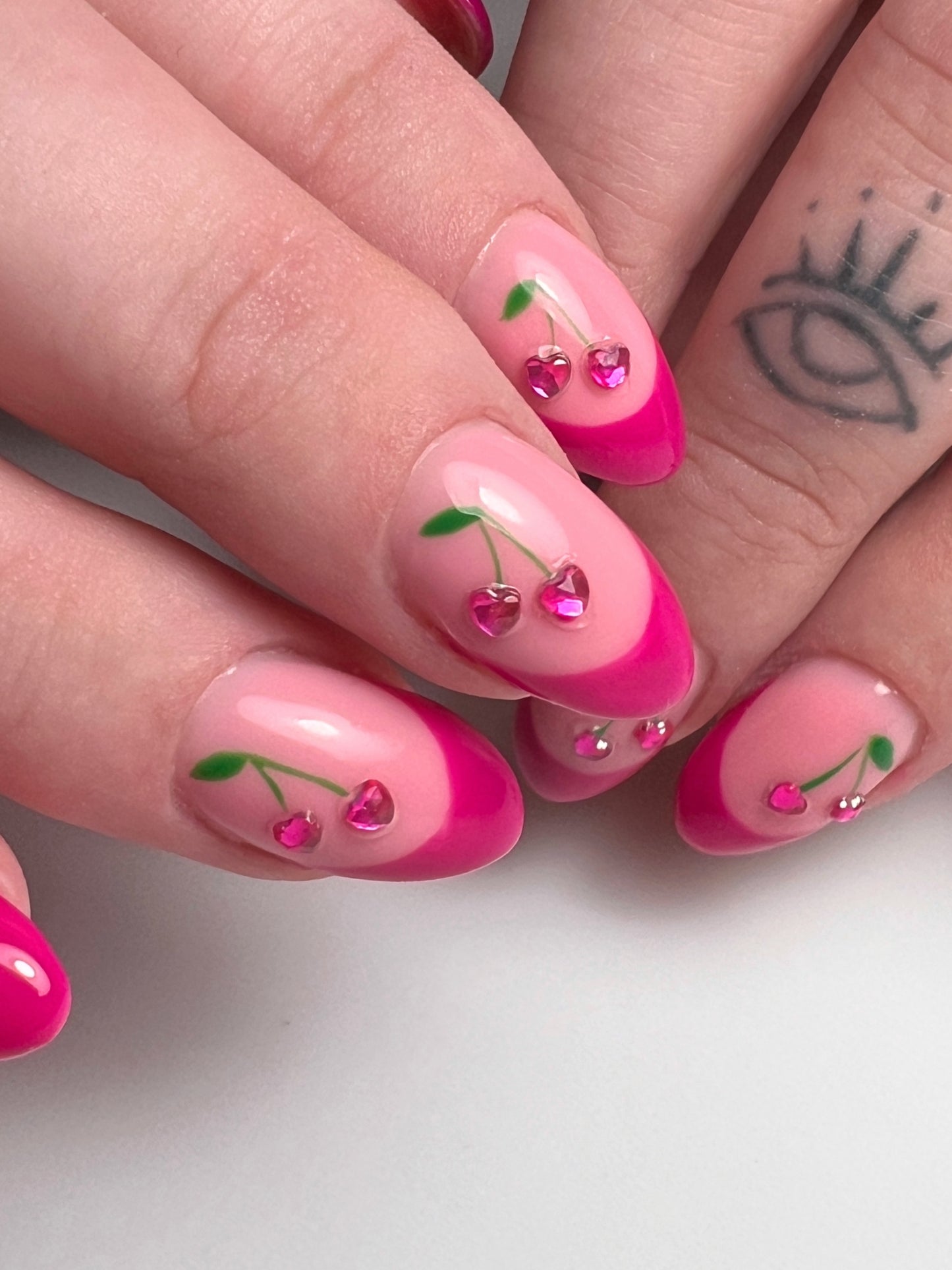 Hands featuring nail art with pink cherry design on neutral background