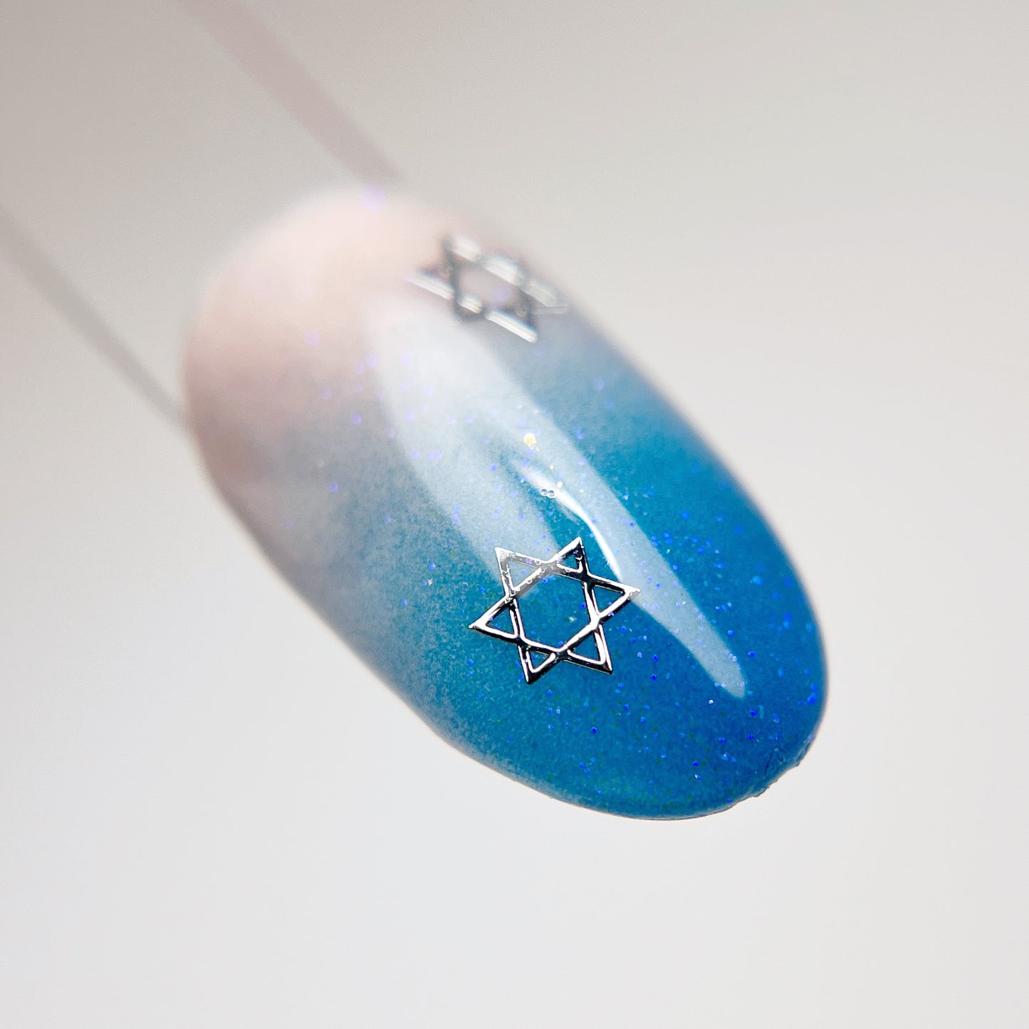 Nail tip swatch with blue gradient design and silver hexagram charm.