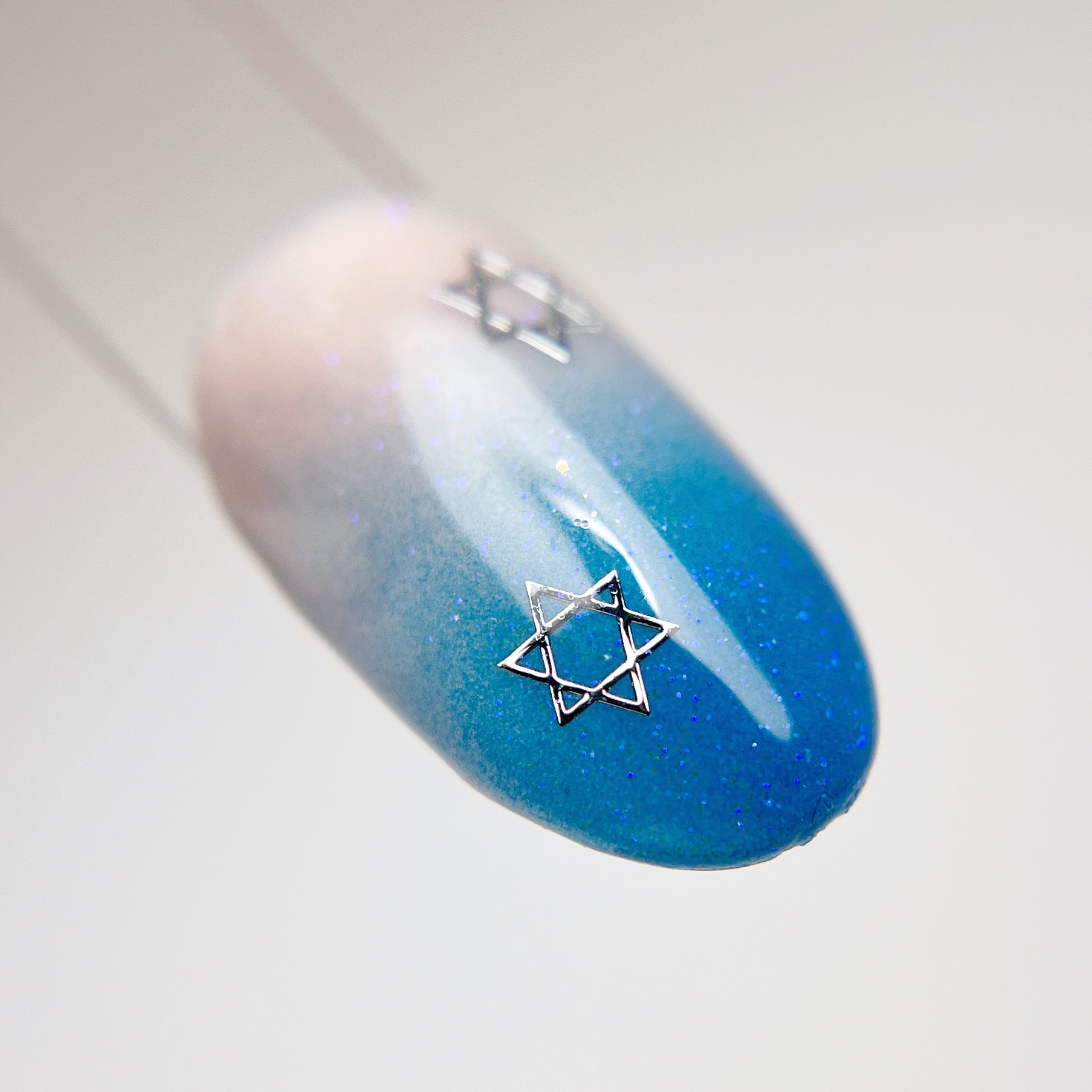 Nail tip swatch with blue gradient design and silver hexagram charm.