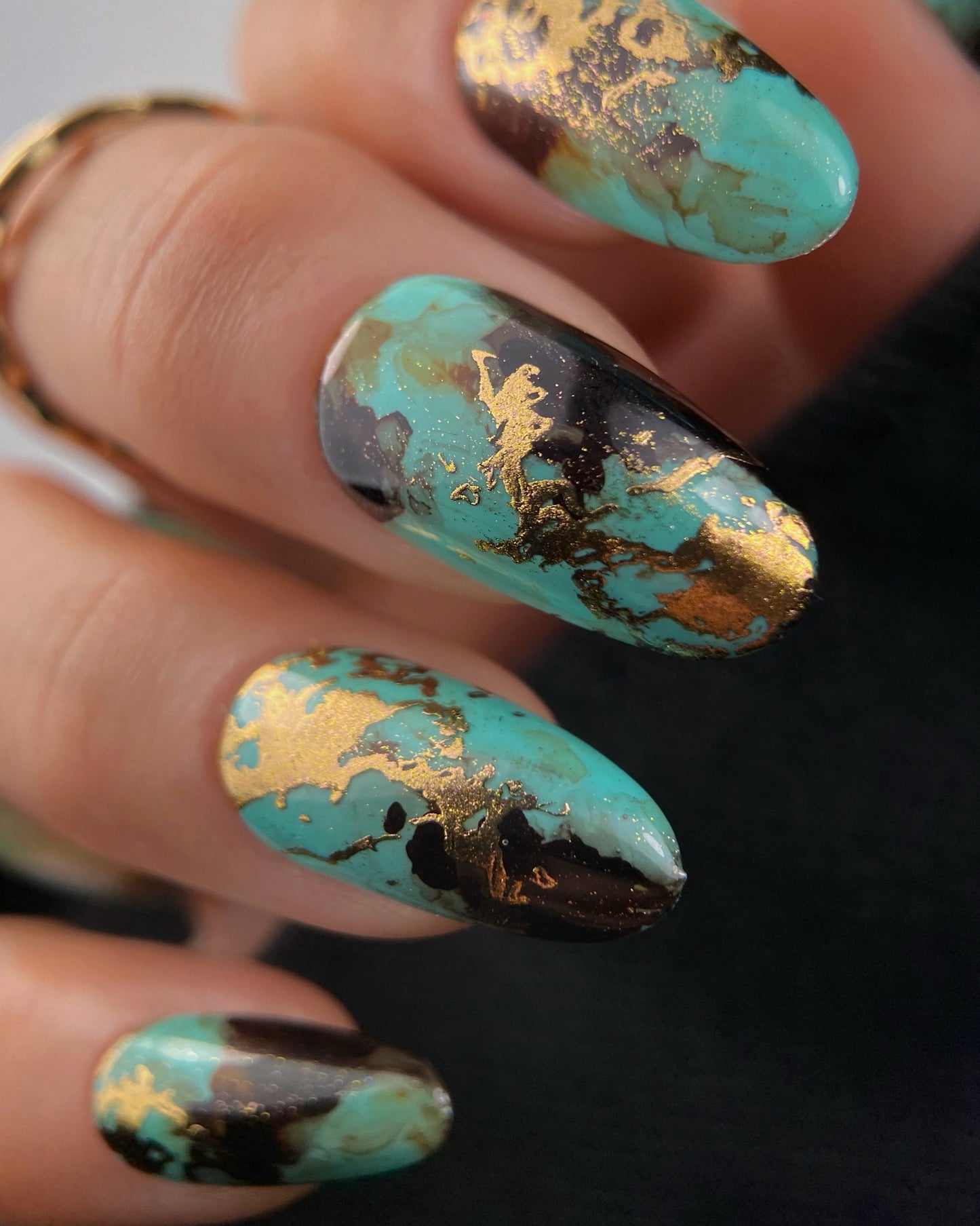 Close-up of a hand with turquoise and gold nail art on a blurred background