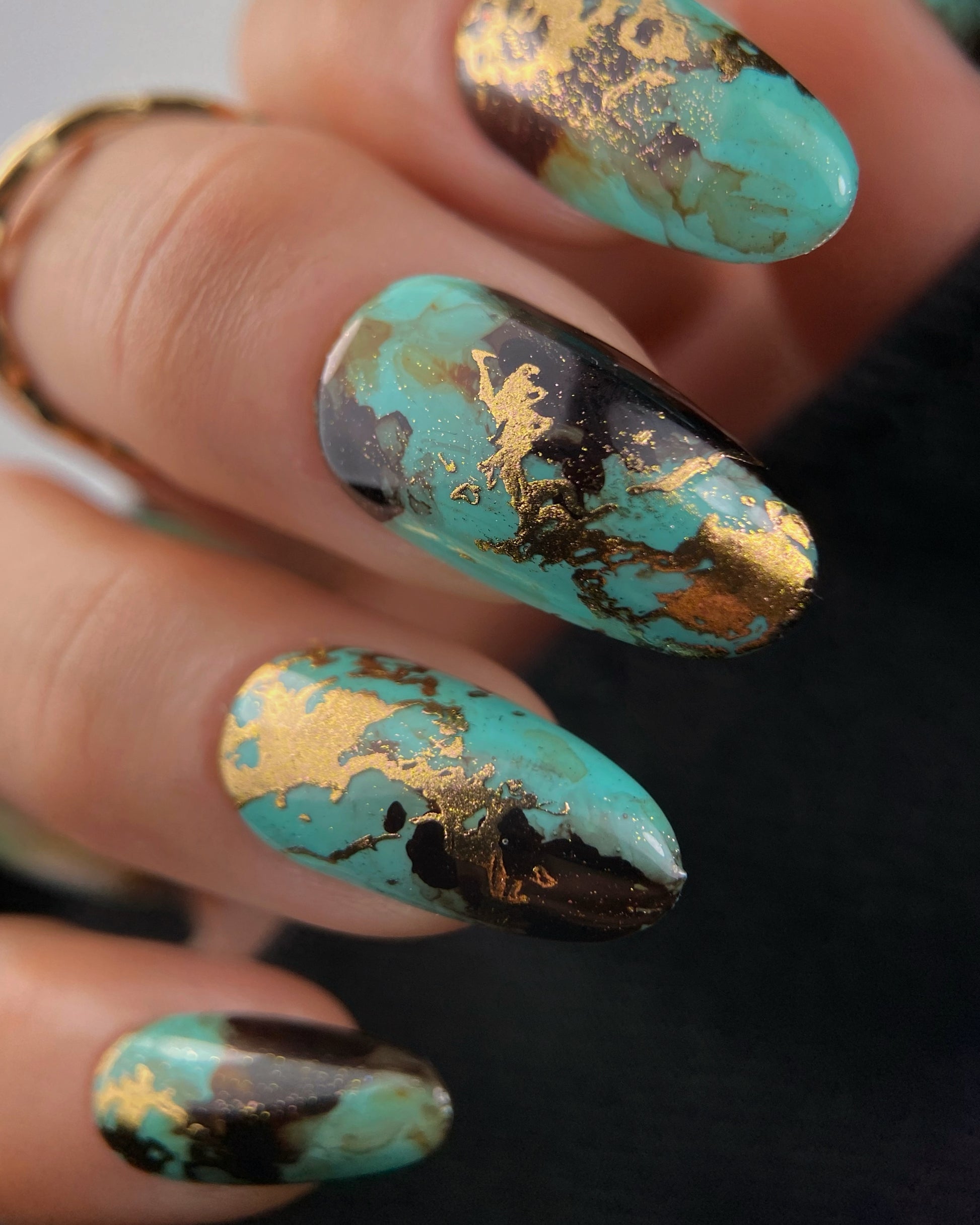 Close-up of a hand with turquoise and gold nail art on a blurred background