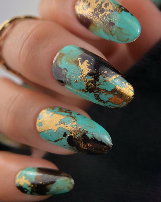Close-up of a hand with turquoise and gold nail art on a blurred background