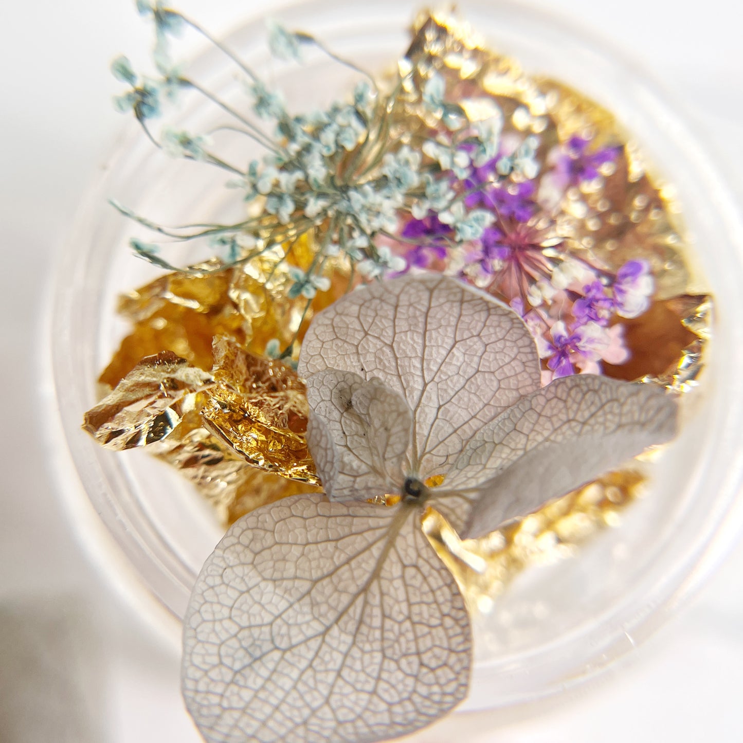 Decorative item with pressed flowers and gold leaf on a white background