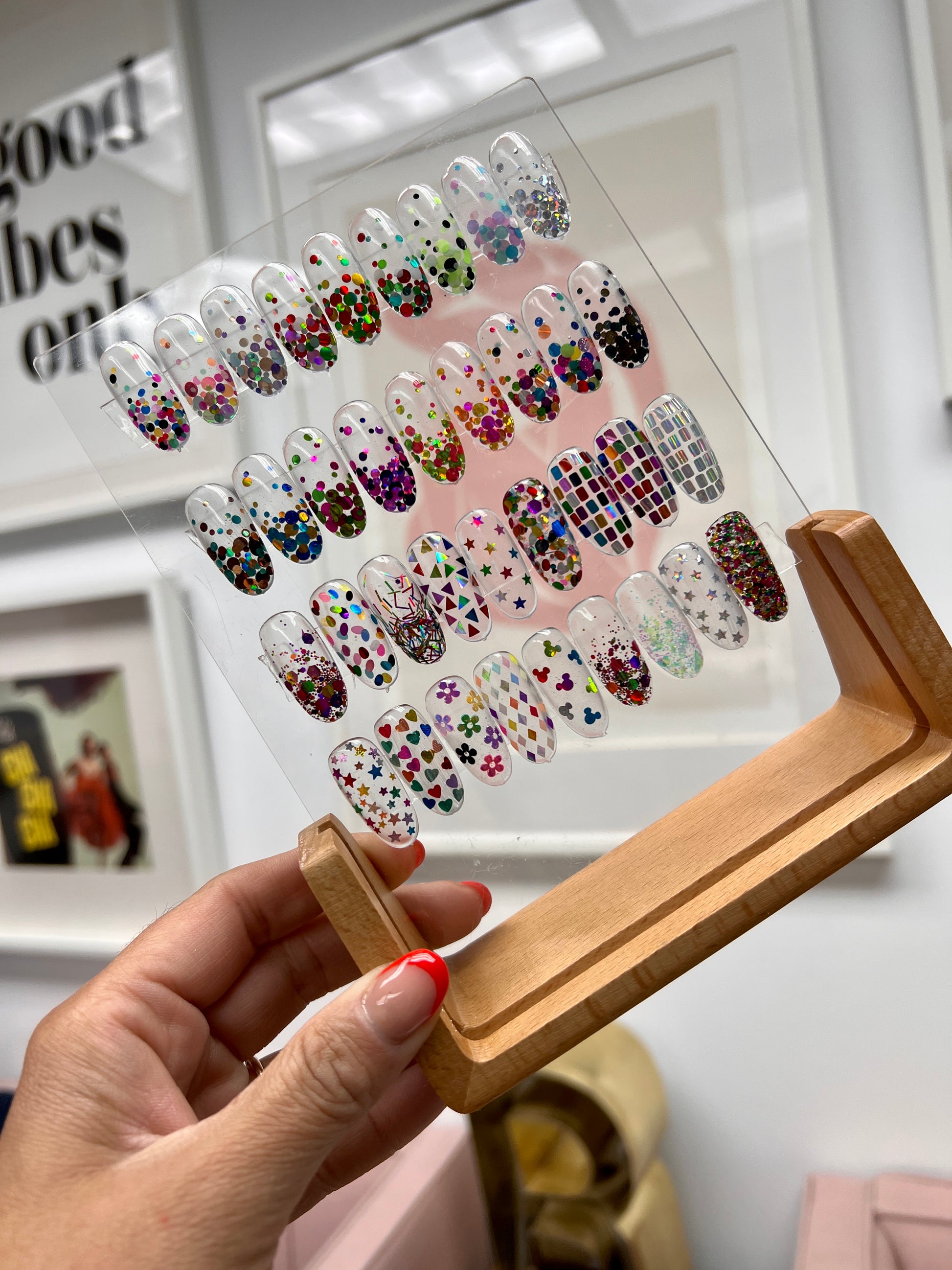 Hand Holding Wood and Clear Acrylic Nail Art Display with Sample Nail Art Tips, Against a White Wall with Picture Frames