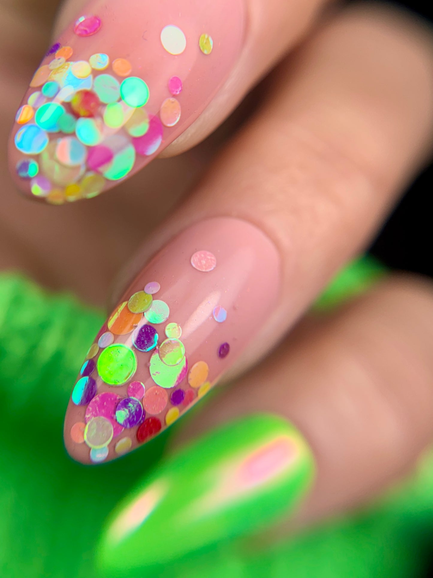 Nails with colorful confetti design on a blurred green background