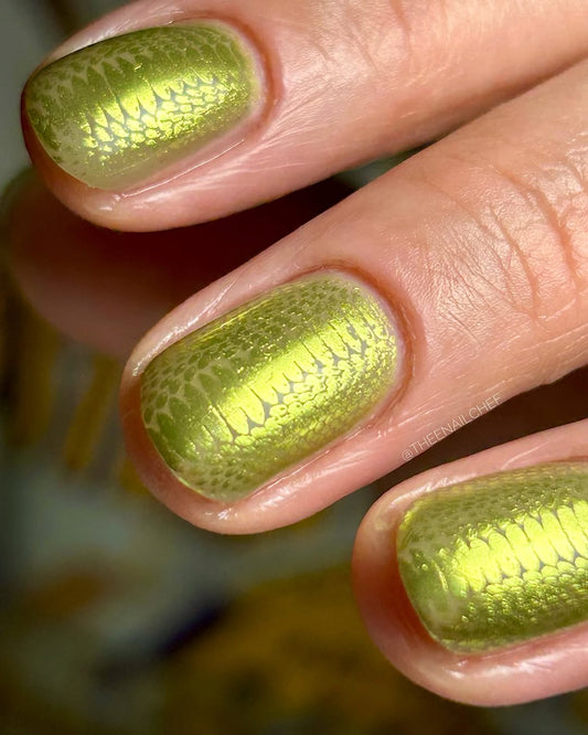 Close-up of a hand with green metallic nail art on a blurred background