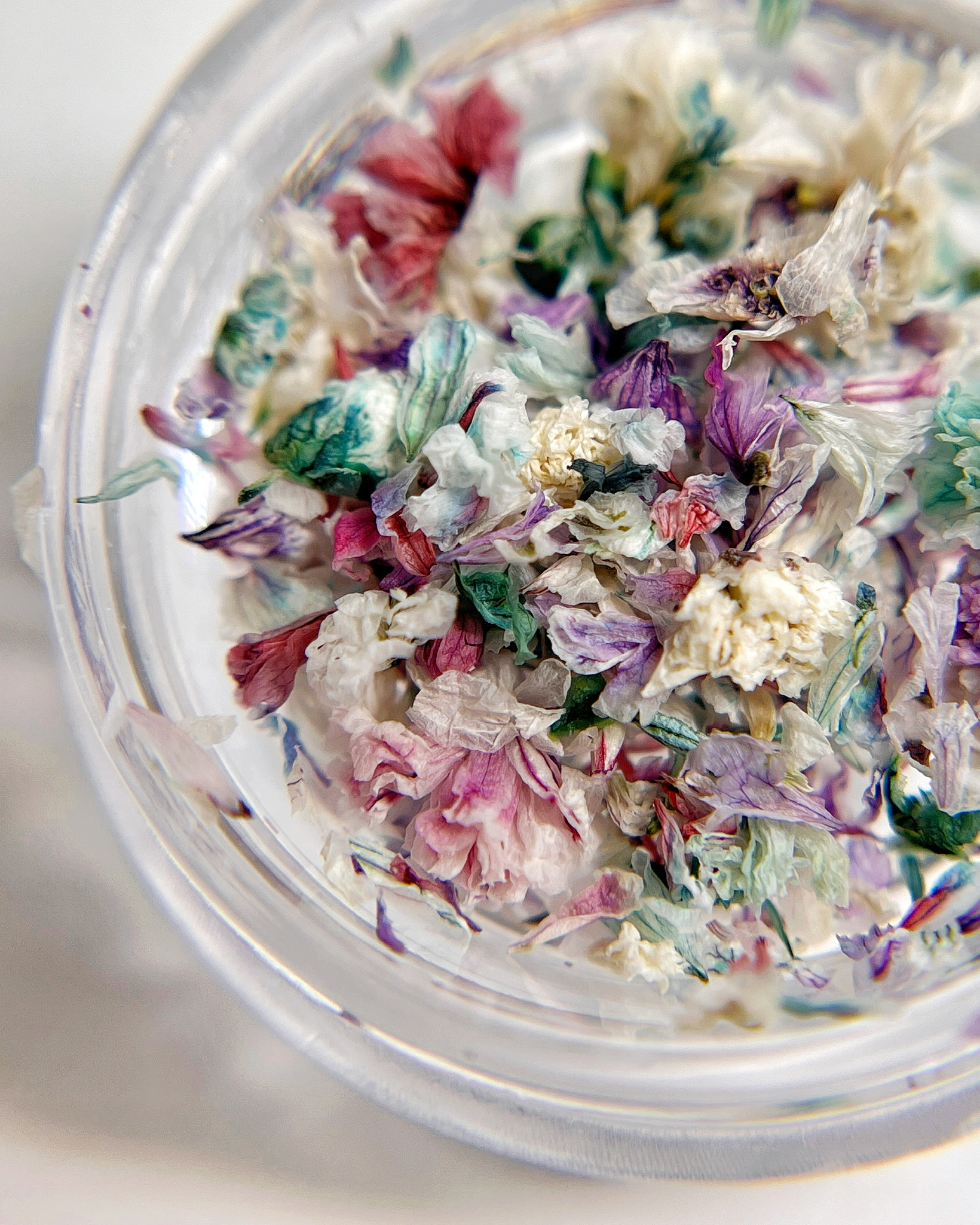 Colorful dried flowers in a clear container on a light background