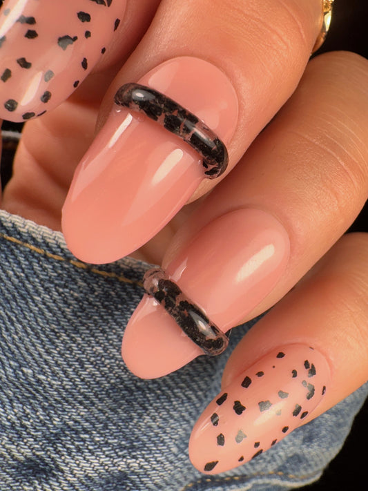 Close-up of nails with black speckled design with clear 3D elements on a denim background