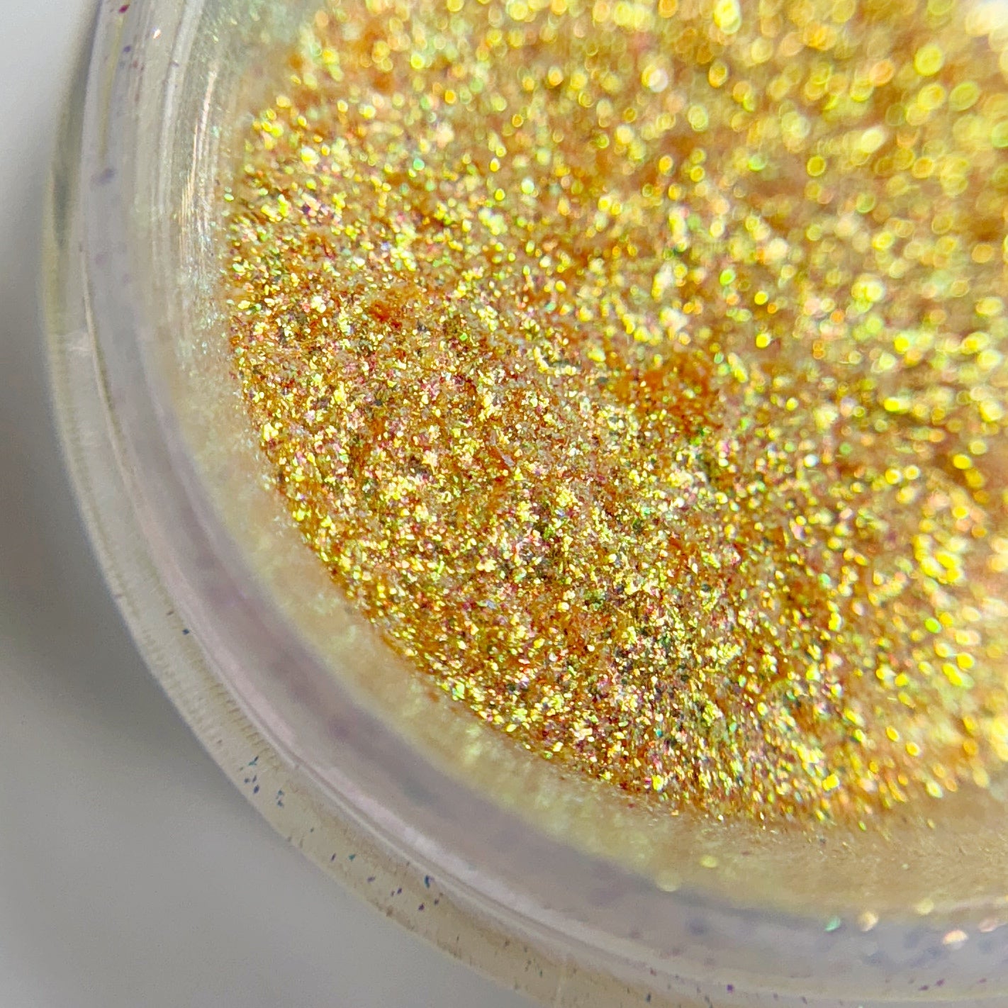A close-up view of a small open jar containing yellow fine glitter, intended for nail art.