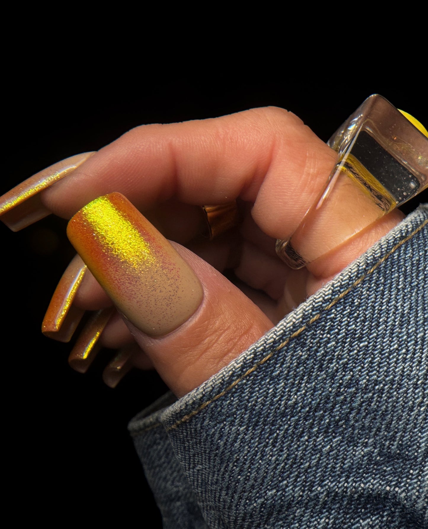 Close-up of a hand with orange gradient nail design and rings on a black background