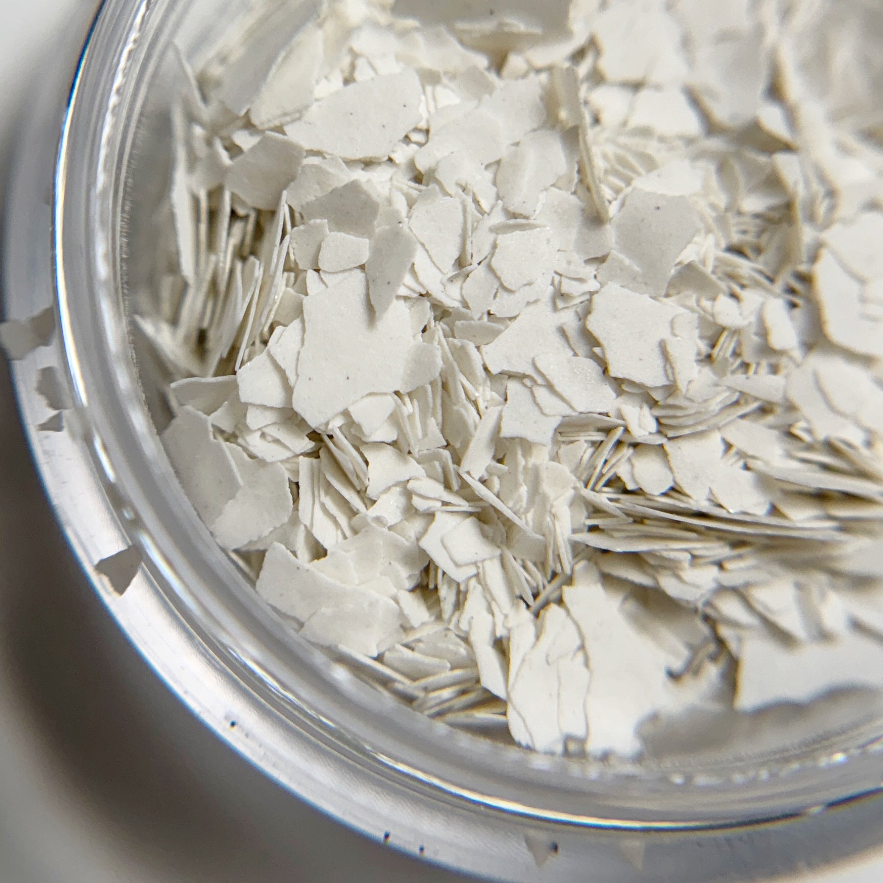 Close up of matte white flakes in jar intended for nail art. 