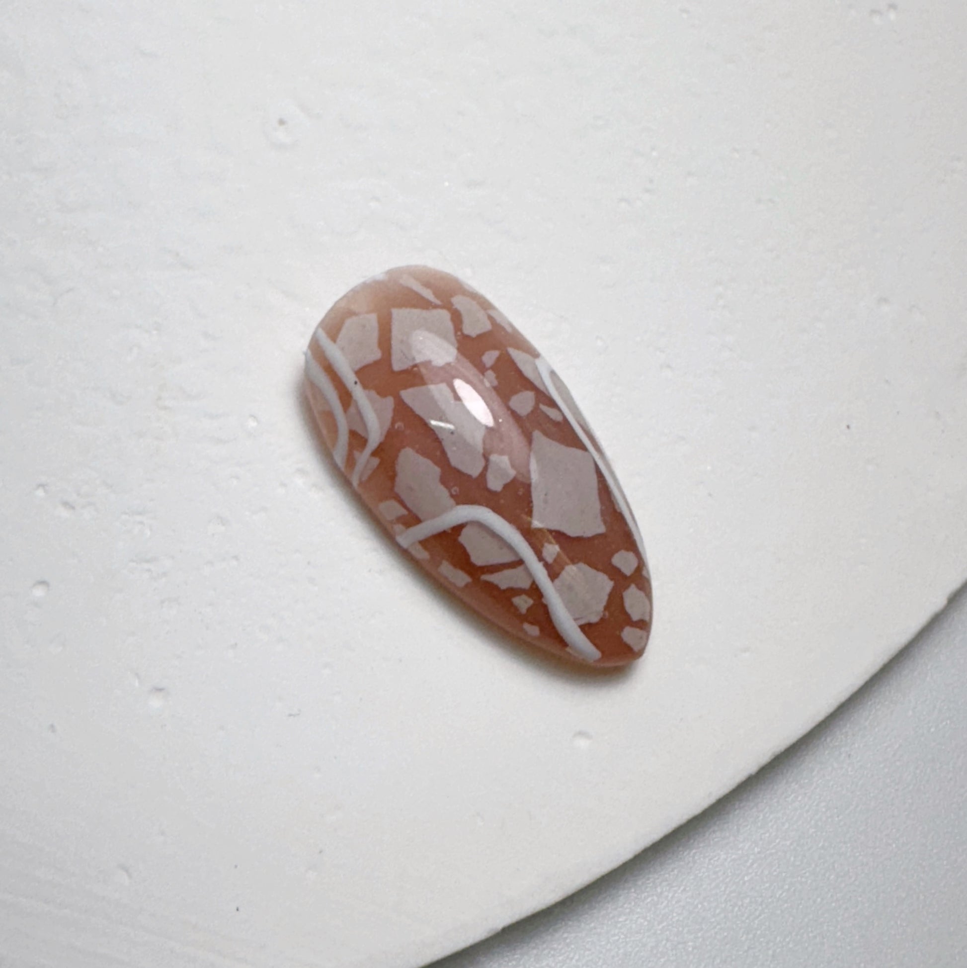 Decorated nail tip on white textured surface.
