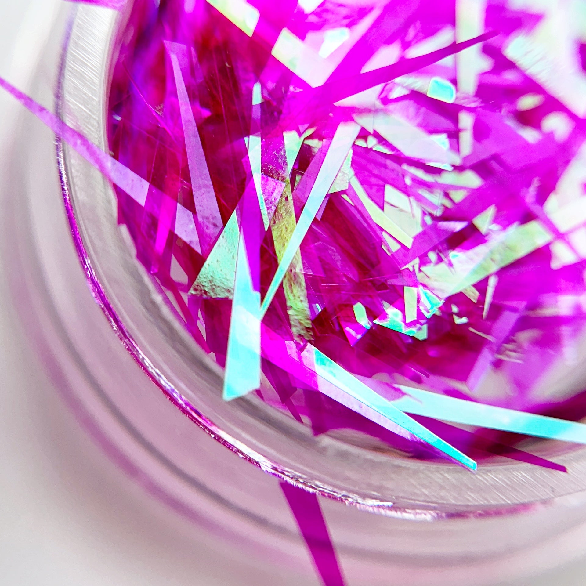 A close-up view of multicolored shattered foil pieces inside a container, intended for nail art.