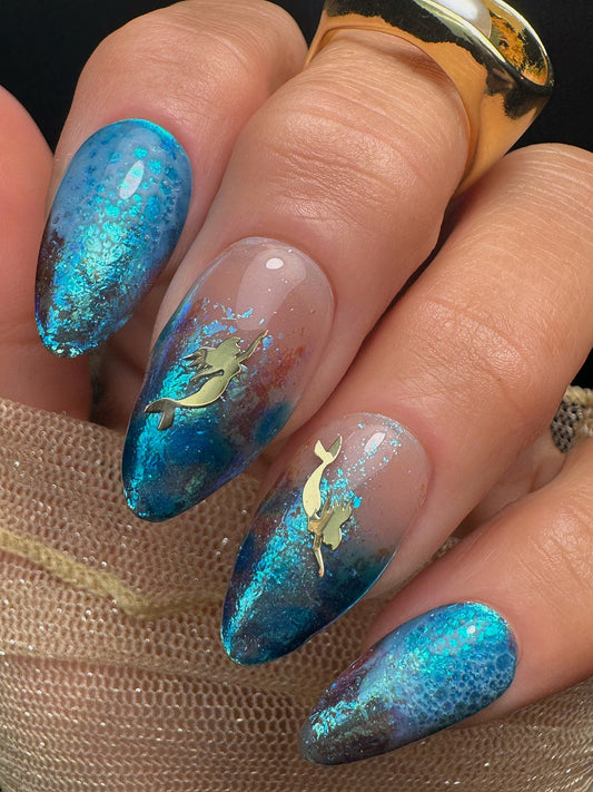 Nails with blue and gold mermaid design held by a hand