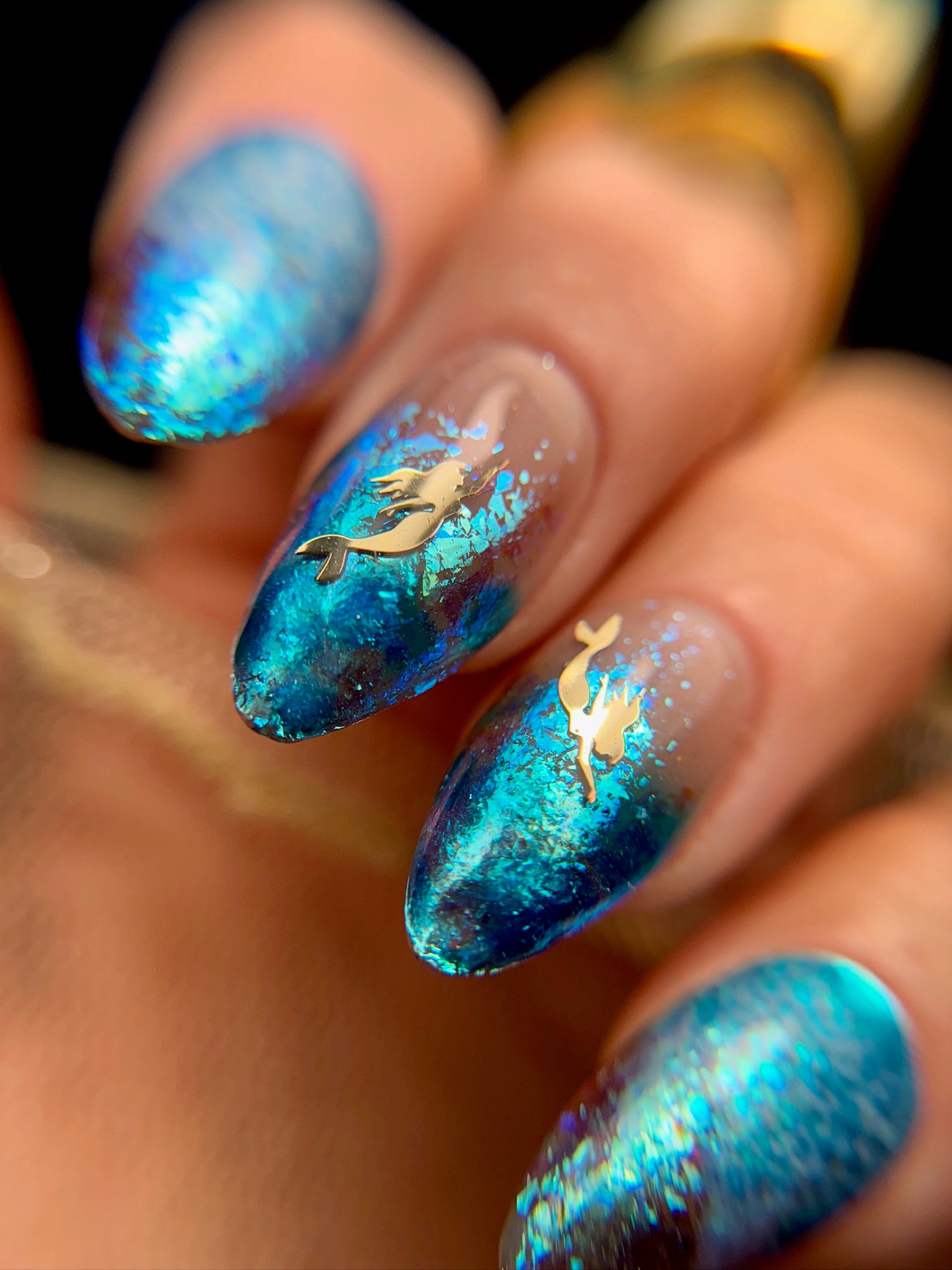 Nails with blue and gold mermaid design on a dark background