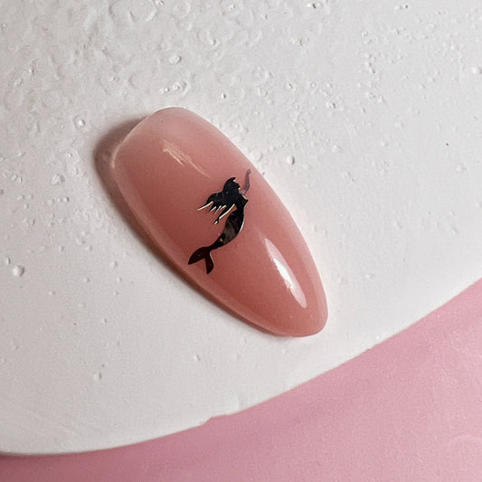 Nail art with a pink nail and silver mermaid silhouette on a light gray background