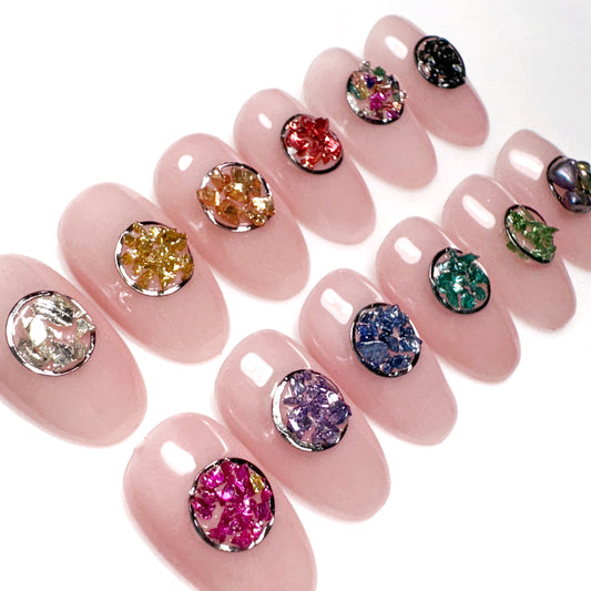 Pink nail tips with colorful gemstones on a white background