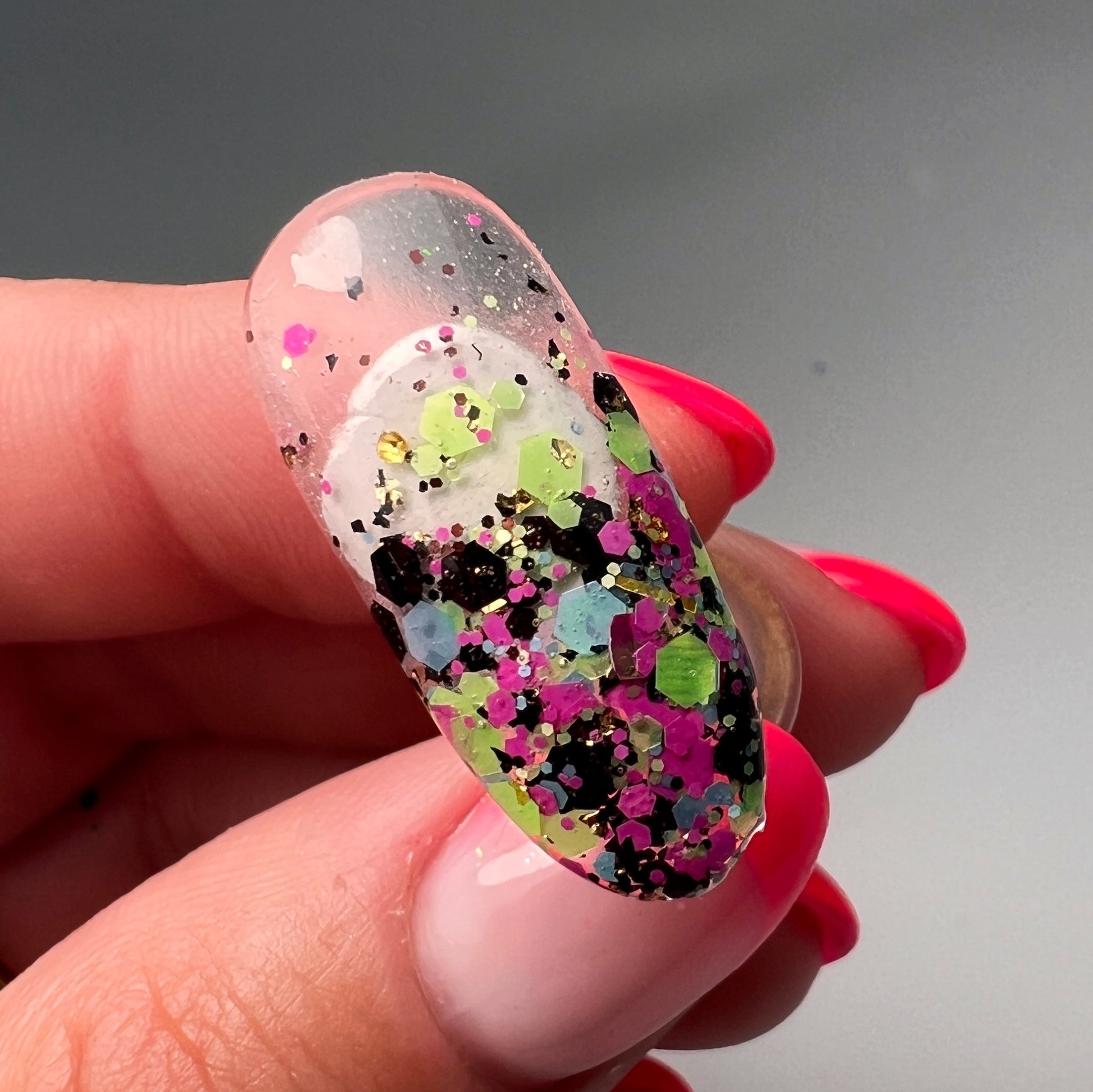 Hand holding decorated nail tip on gray bcakground. 