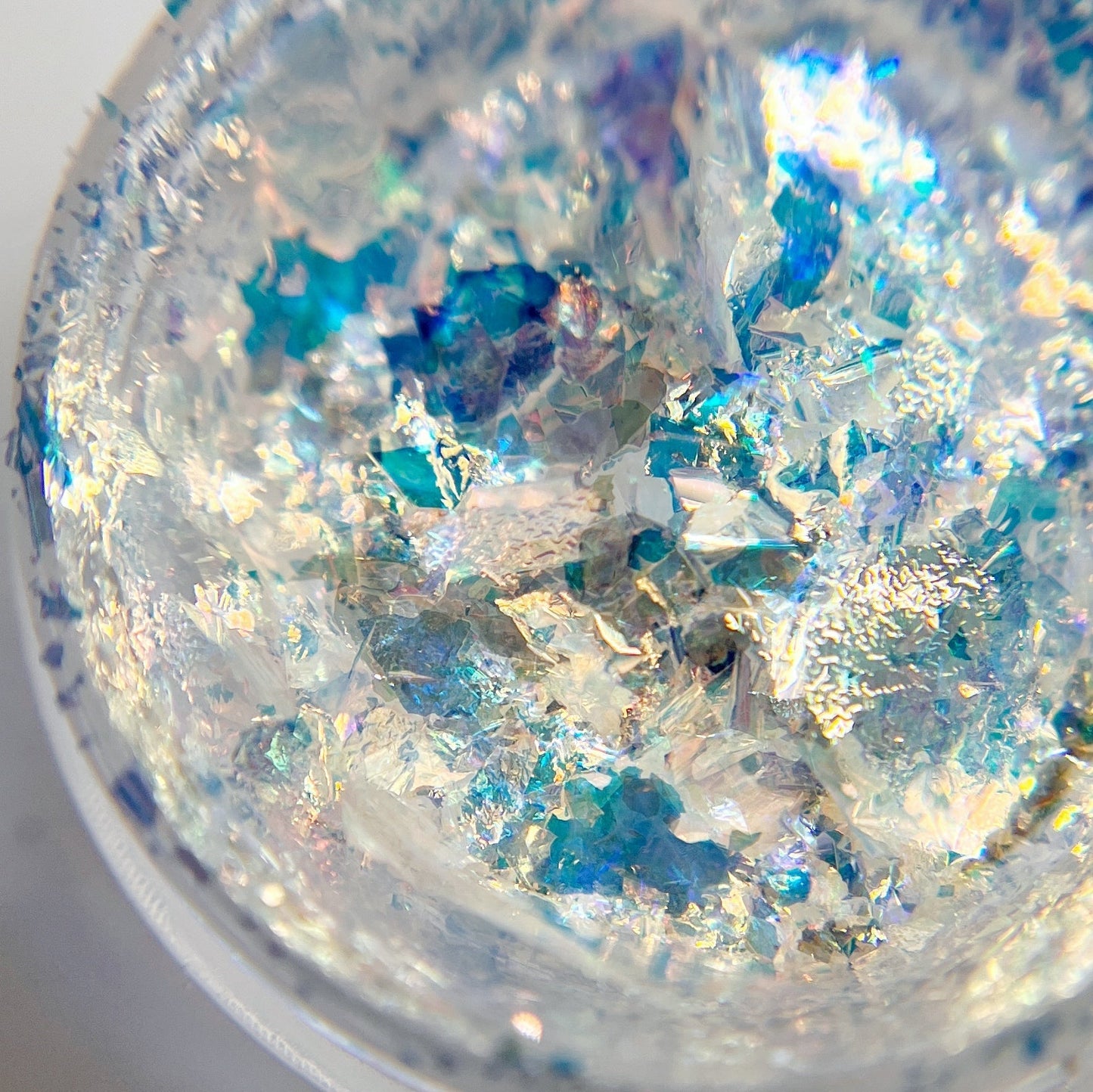 A close-up view of Moon Fluff flake nail art flakes, showcasing a mix of soft blue and opalescent golden colors.