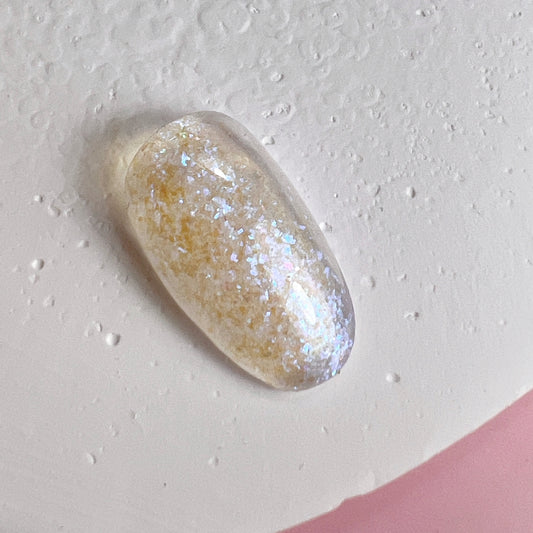 Close up of nail tip with glittery finish on textured white surface and pink background.