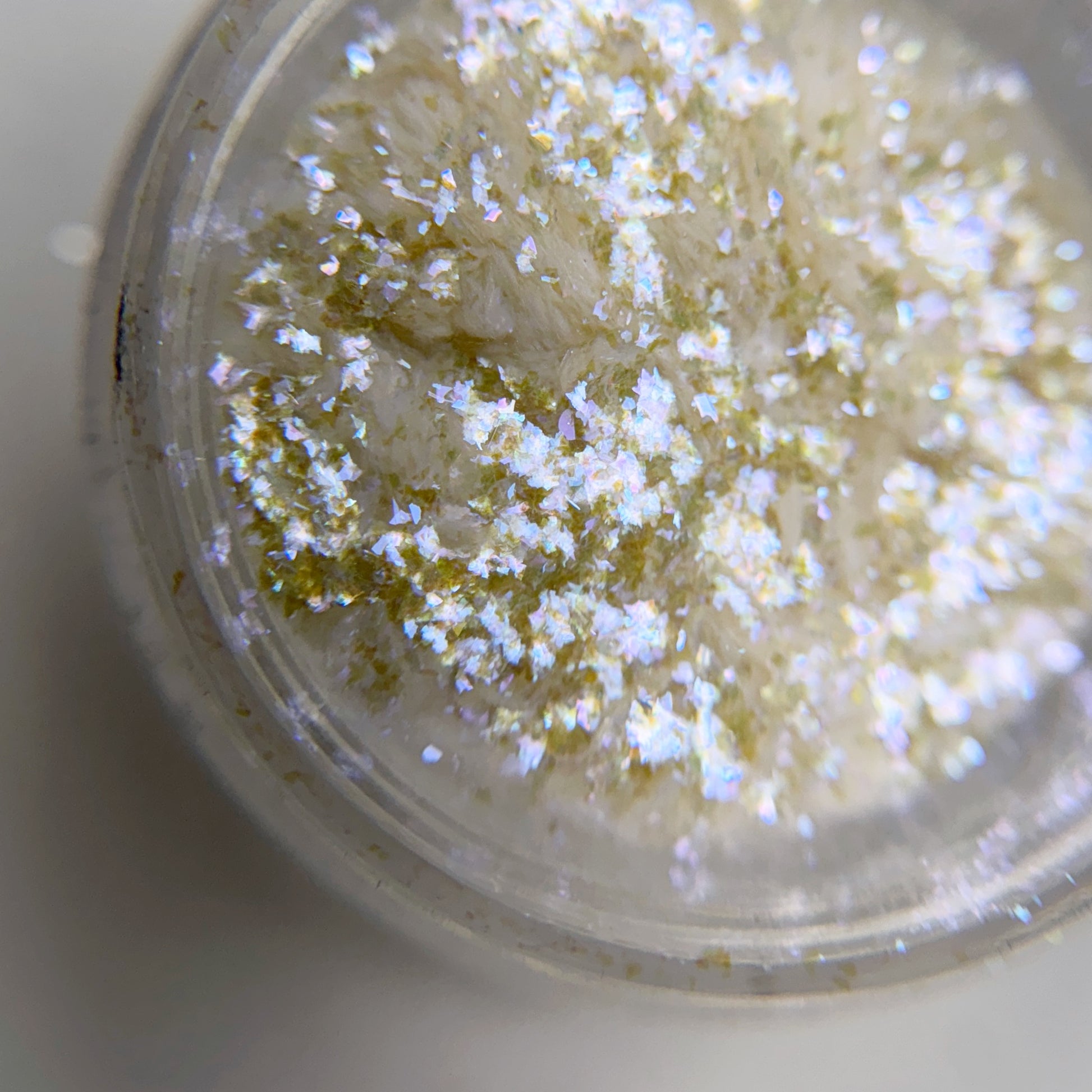 Close up of iridescent flakes in transparent jar on blurred background.
