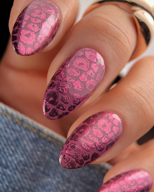 Close-up of a hand with burgundy metallic nail design on a denim background