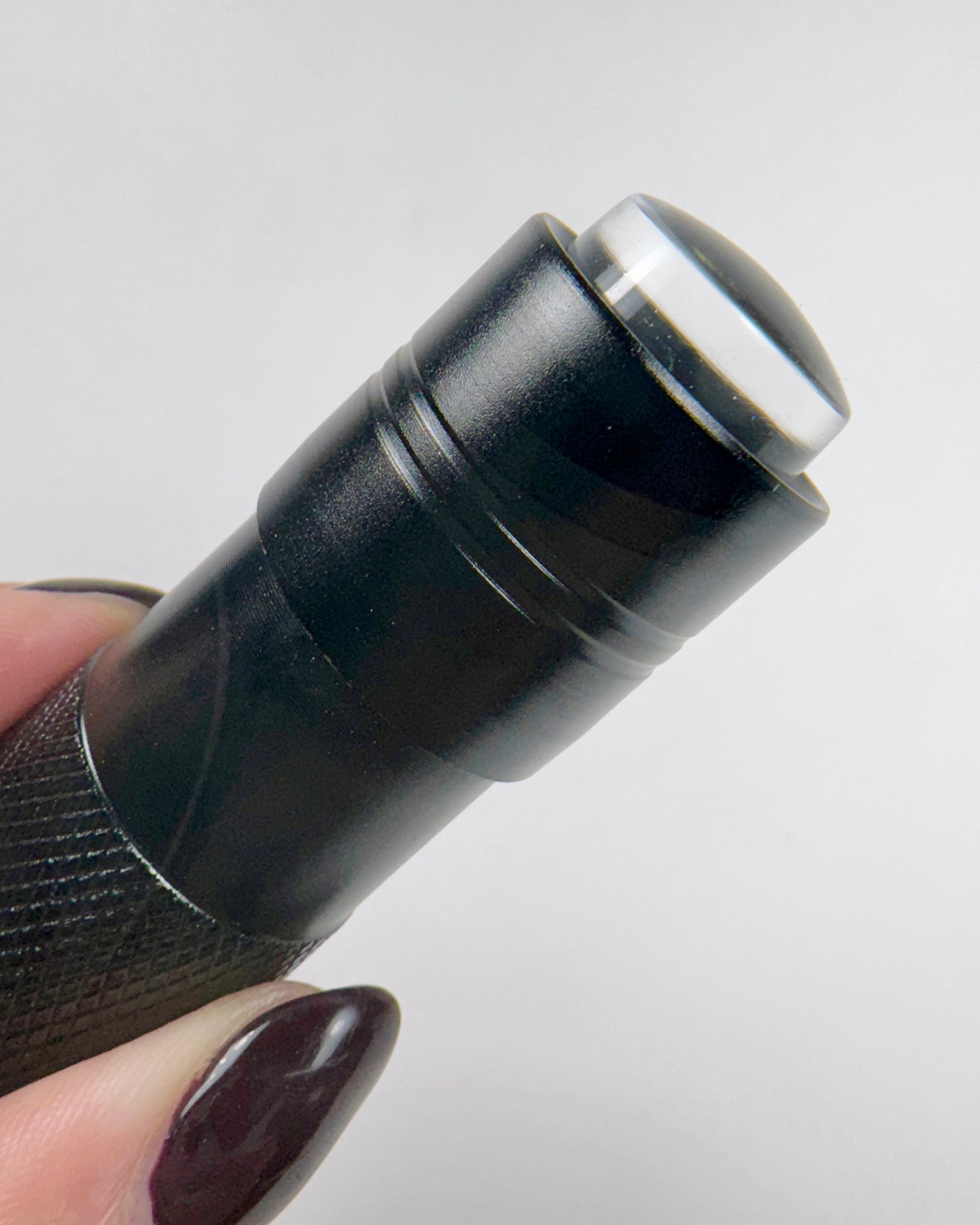 Close-up of a black flash cure light held by a hand with dark nail polish on a light gray background.