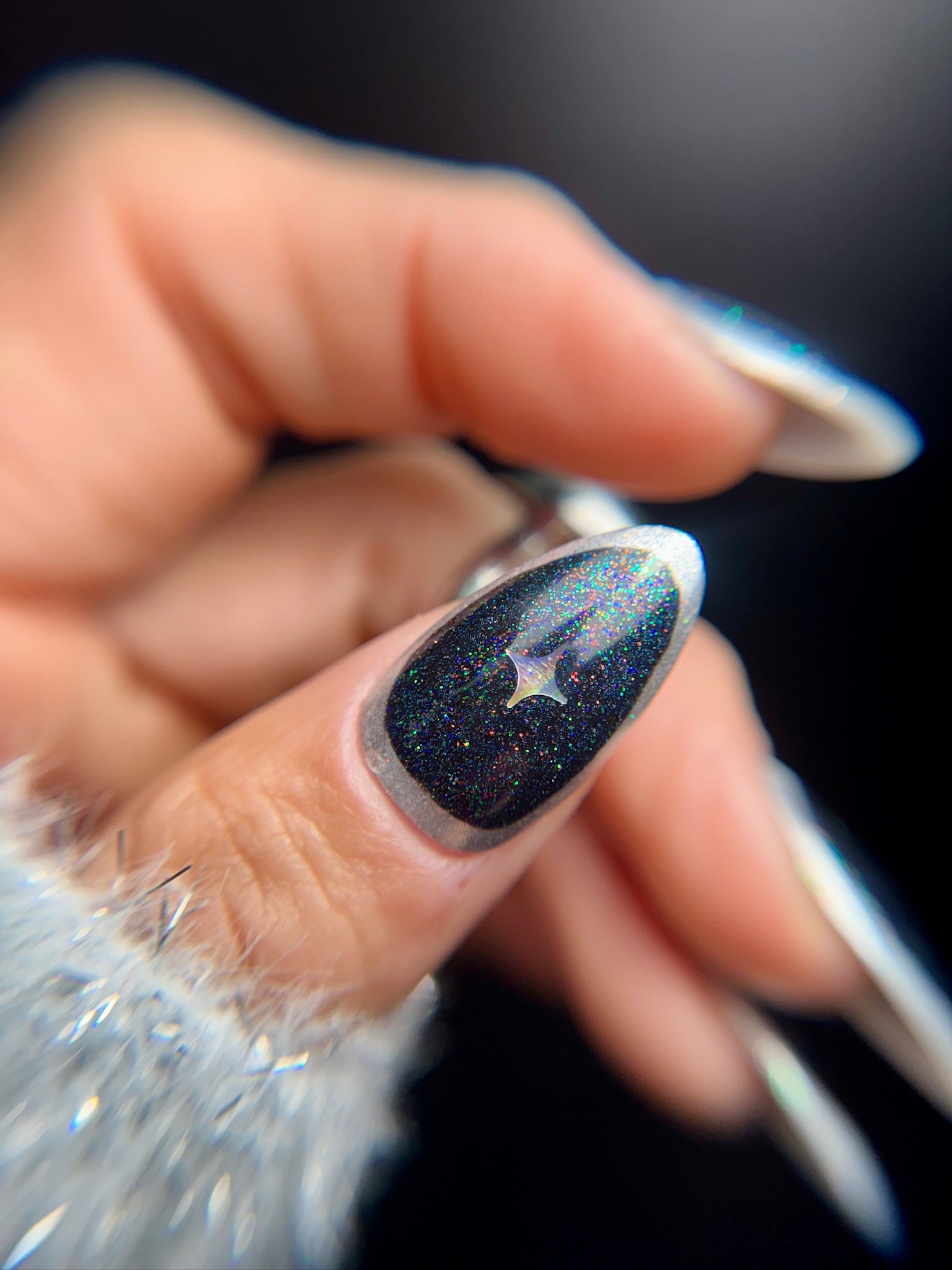 Close-up of a hand with a starry night-themed nail design against a dark background