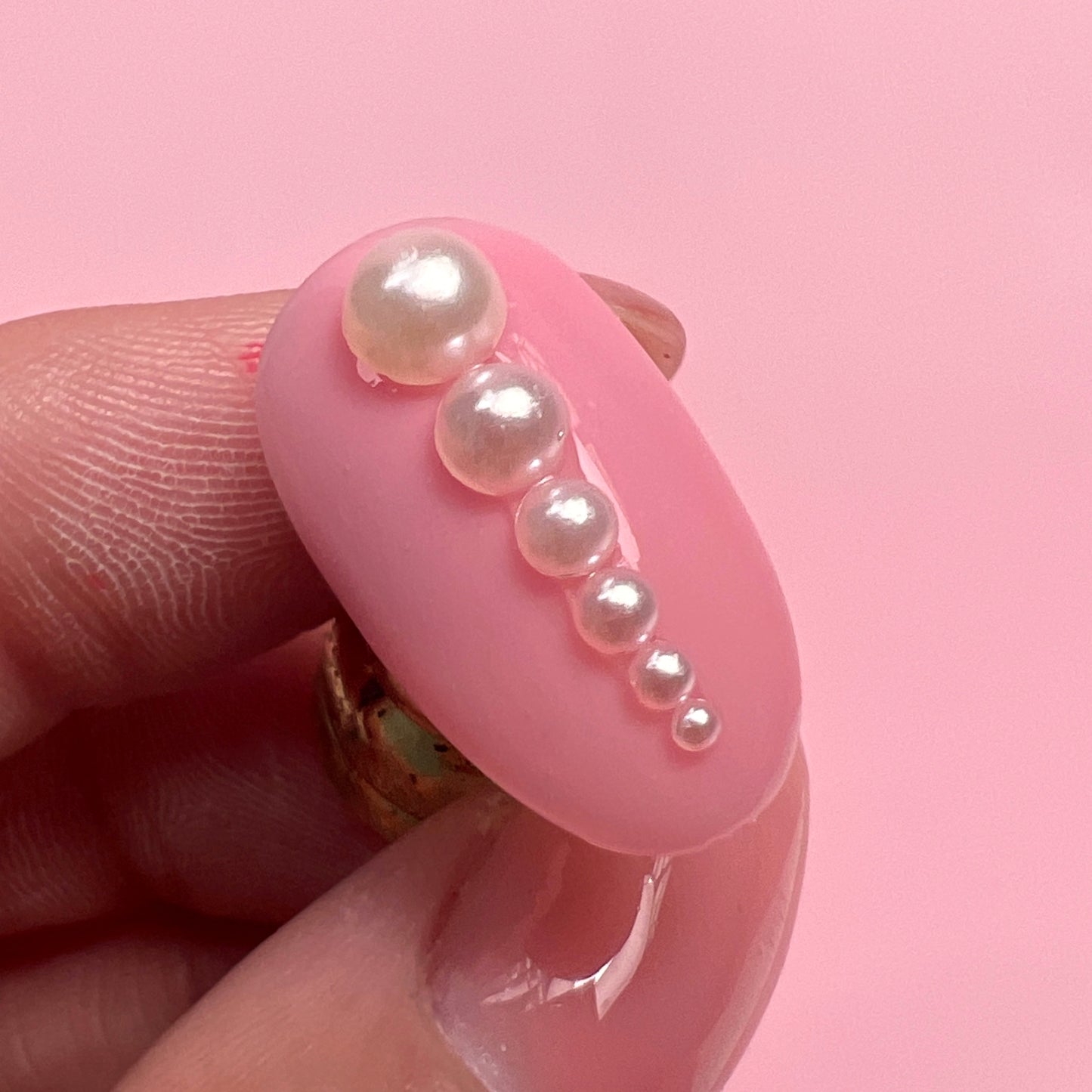 Hand holding decorated nail tip against pink background.