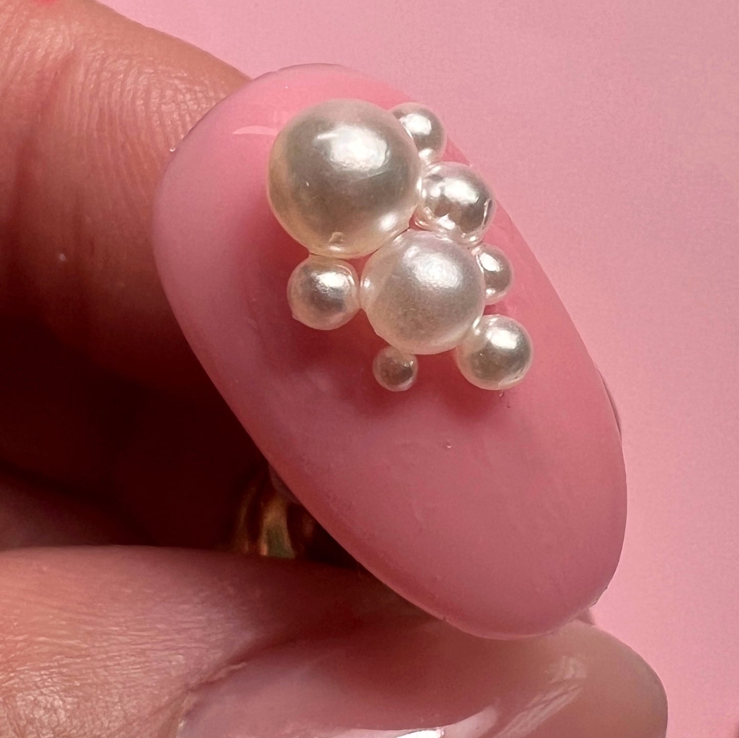 Hand holding decorated nail tip against pink background.